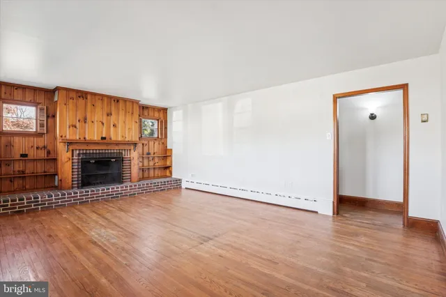 an empty room with wooden floor fireplace and windows