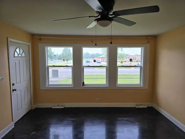 an empty room with wooden floor fan and windows