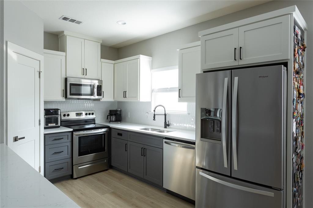 1108 Claude Street Dallas, TX 75203 - Photo 8 of 17 Modern kitchen featuring two-tone cabinetry with white upper and charcoal lower cabinets, stainless steel appliances, a white subway tile backsplash, white countertops, and wood-finish flooring