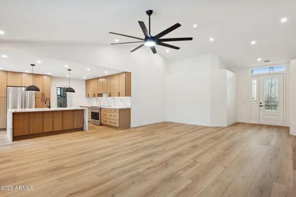a view of an empty room with wooden floor and a kitchen