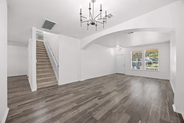 an empty room with wooden floor chandelier fan and windows