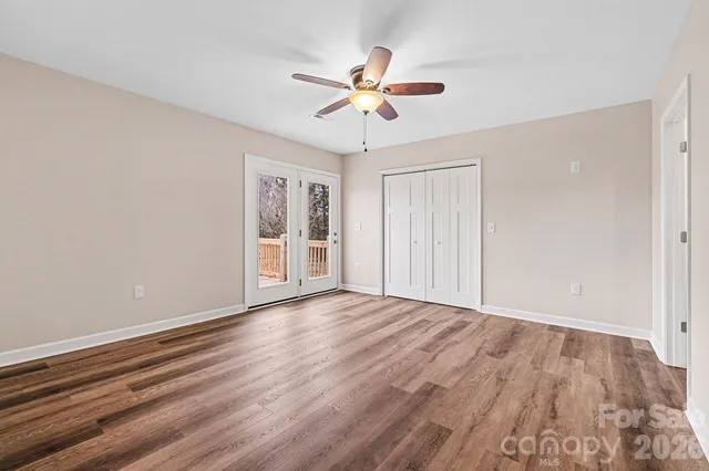 a view of an empty room with wooden floor and a ceiling fan