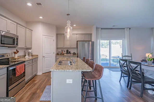 a kitchen with stainless steel appliances granite countertop a stove top oven a refrigerator a sink and chairs