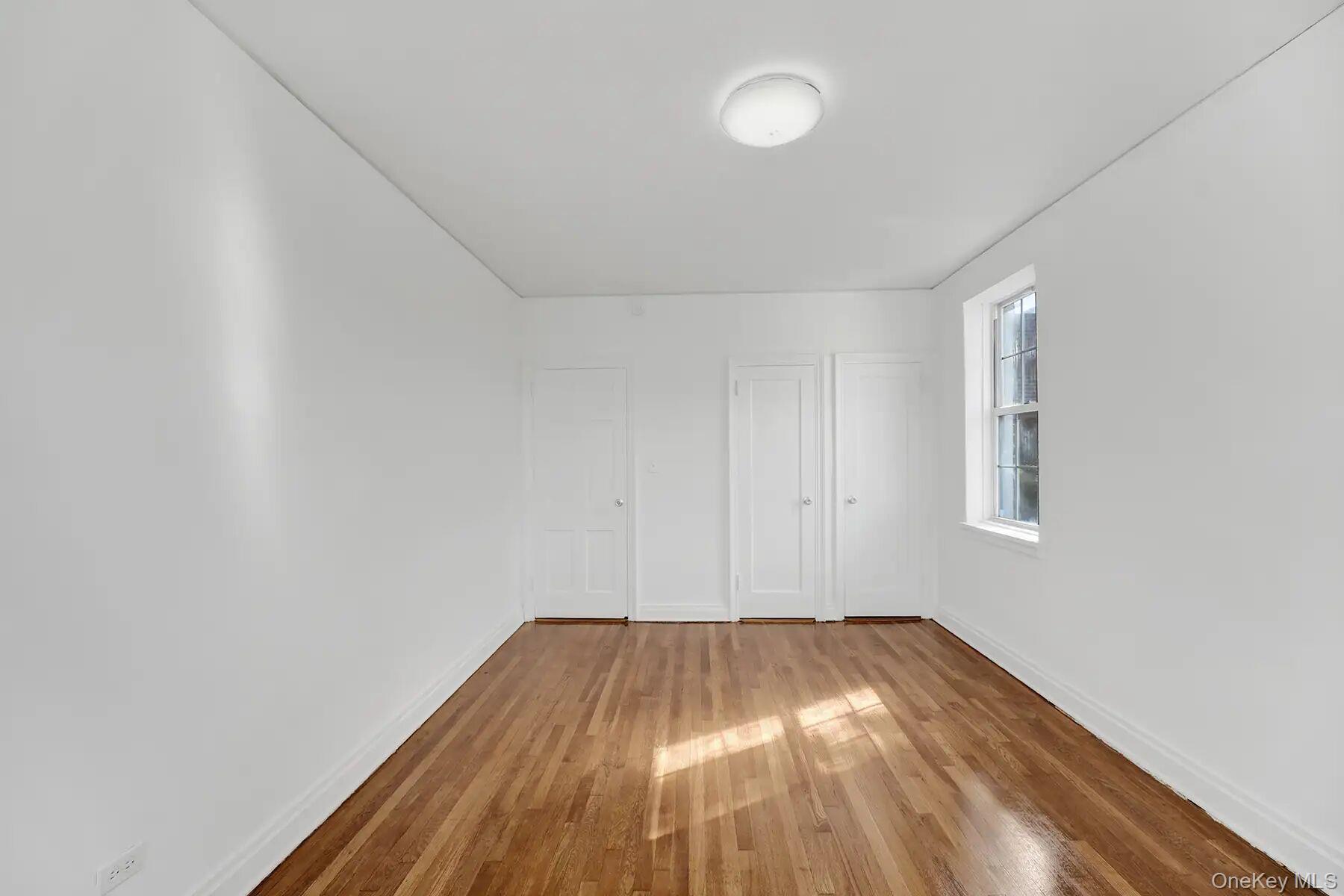 1 Ash Place, Unit 3A Great Neck, NY 11021 - Photo 9 of 10 Bright room featuring wood-finish flooring, white walls, two panel doors, and a double-hung window