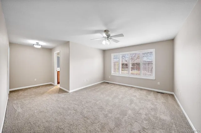 an empty room with chandelier fan and windows