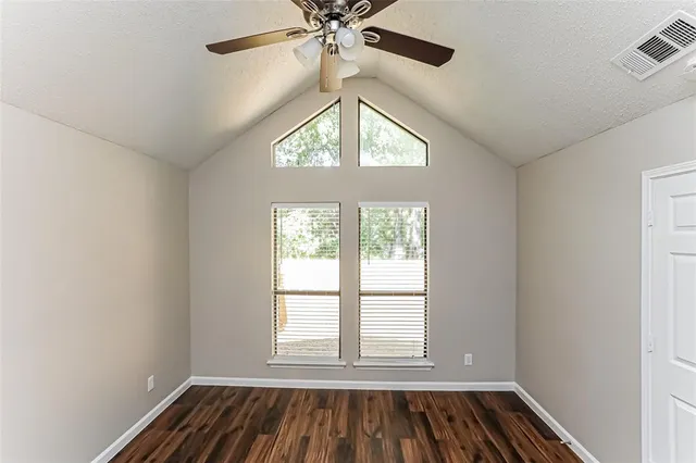 an empty room with wooden floor fan and windows