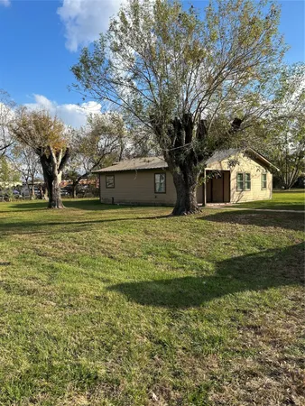 a view of a white house next to a yard with a large tree
