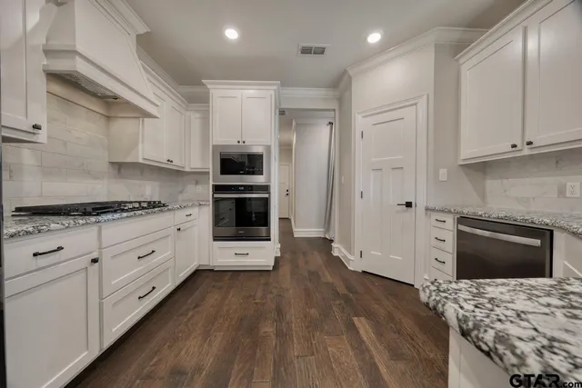 a kitchen with stainless steel appliances kitchen island granite countertop a stove a sink and white cabinets