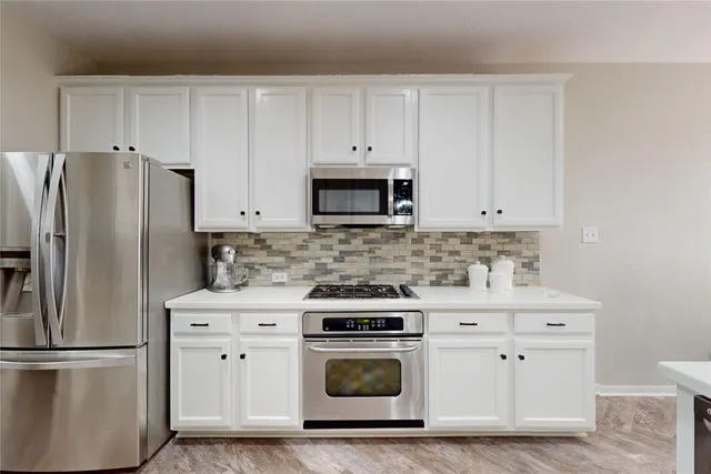 a kitchen with stainless steel appliances granite countertop a refrigerator a sink a stove a dining table and chairs with wooden floor