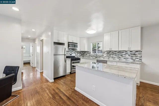 a kitchen with stainless steel appliances granite countertop a refrigerator a sink a stove and white cabinets with wooden floor