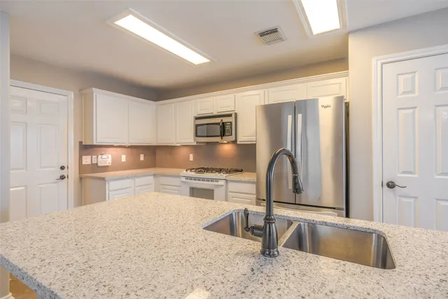 a kitchen with granite countertop a sink stainless steel appliances and white cabinets