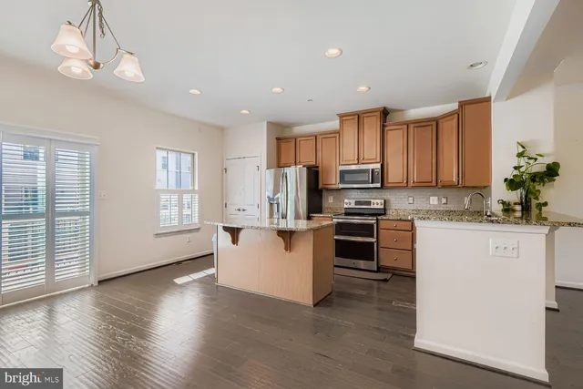 a kitchen with stainless steel appliances granite countertop a refrigerator a stove top oven a sink cabinets and wooden floor