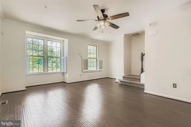 an empty room with wooden floor chandelier fan and windows