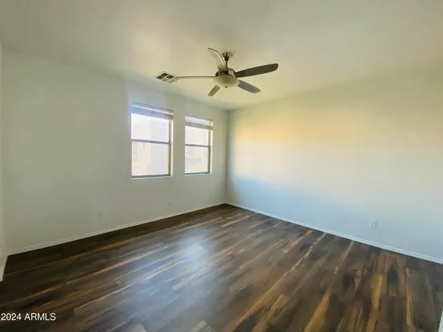 an empty room with wooden floor fan and windows