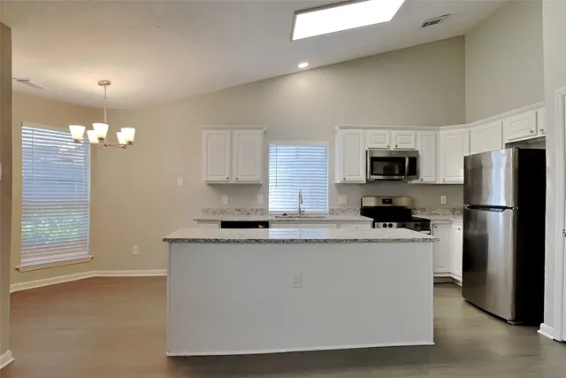 a kitchen with kitchen island granite countertop stainless steel appliances a sink a stove a refrigerator cabinets and a window