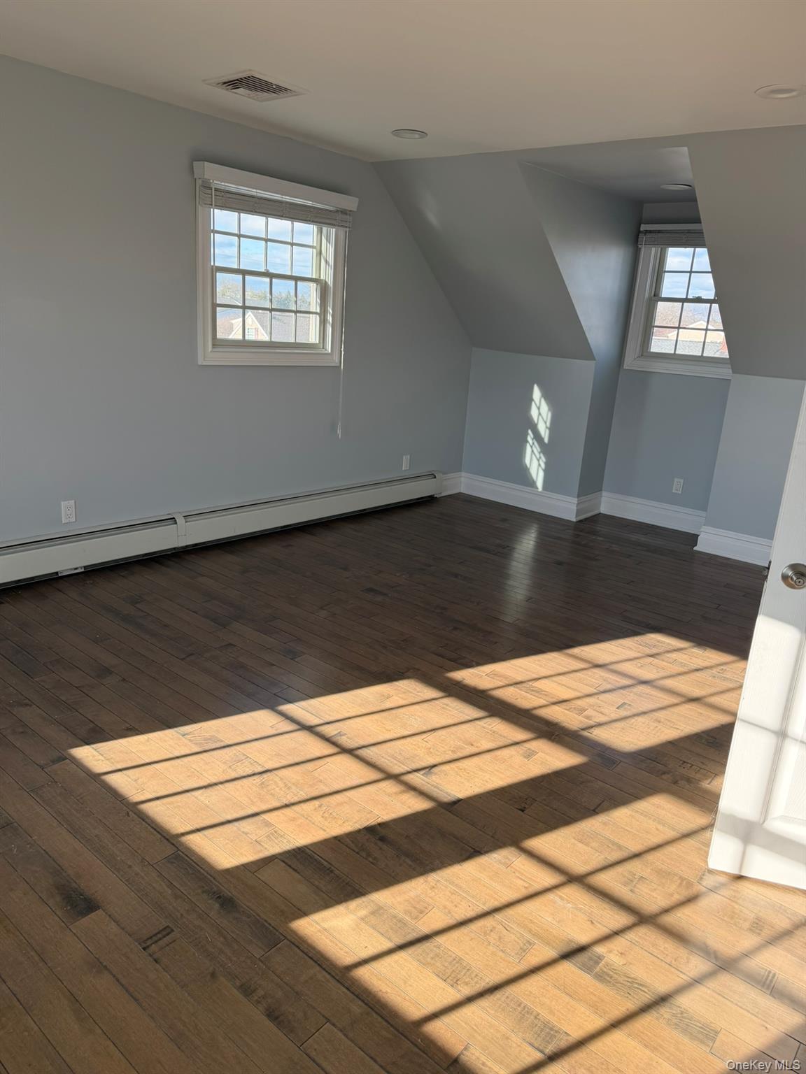 16 Cape Road Amityville, NY 11701 - Photo 19 of 27 Additional living space featuring baseboard heating, plenty of natural light, dark wood finished floors, and lofted ceiling