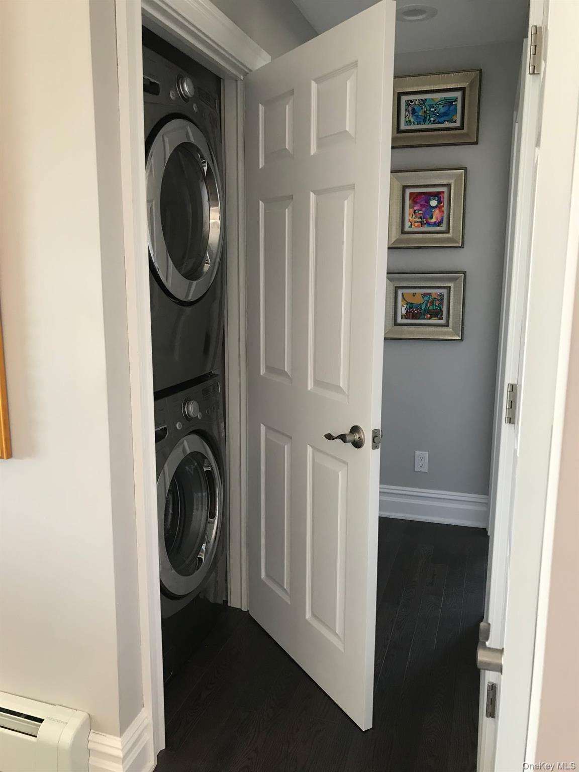 16 Cape Road Amityville, NY 11701 - Photo 23 of 27 Washroom with dark wood-style floors, stacked washer and clothes dryer, and baseboard heating