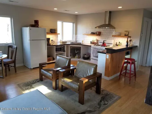a living room with stainless steel appliances furniture a rug kitchen view and a large window