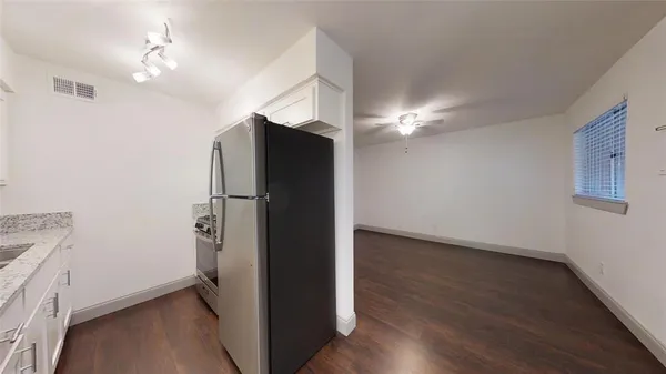 a view of a refrigerator in kitchen and an empty room with wooden floor