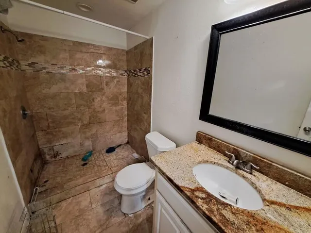 a bathroom with a granite countertop sink toilet a mirror and shower
