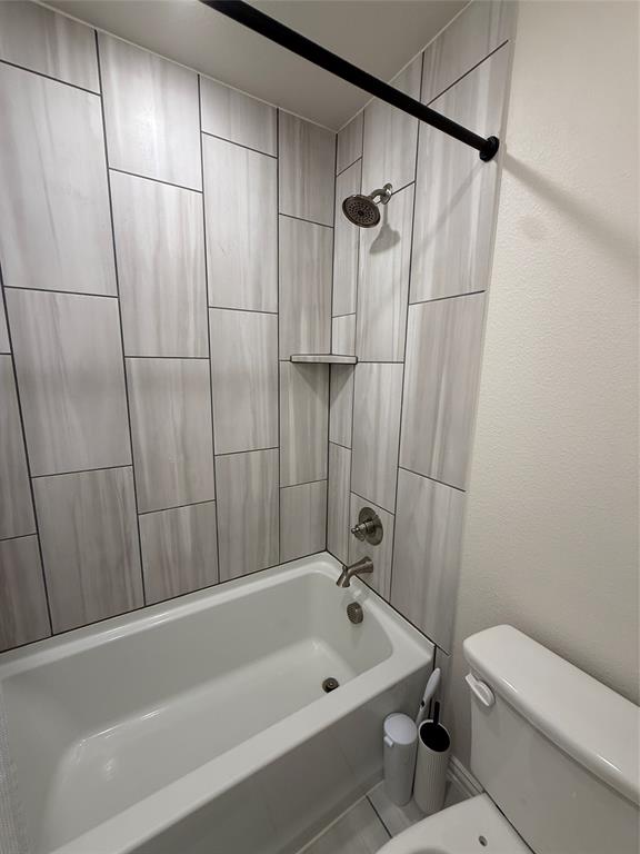 5212 Troupe Road McKinney, TX 75071 - Photo 21 of 38 Bathtub shower combination featuring light-toned rectangular wall tiles with contrasting grout, a built-in shower shelf, brushed nickel showerhead and faucet, and a black shower rod