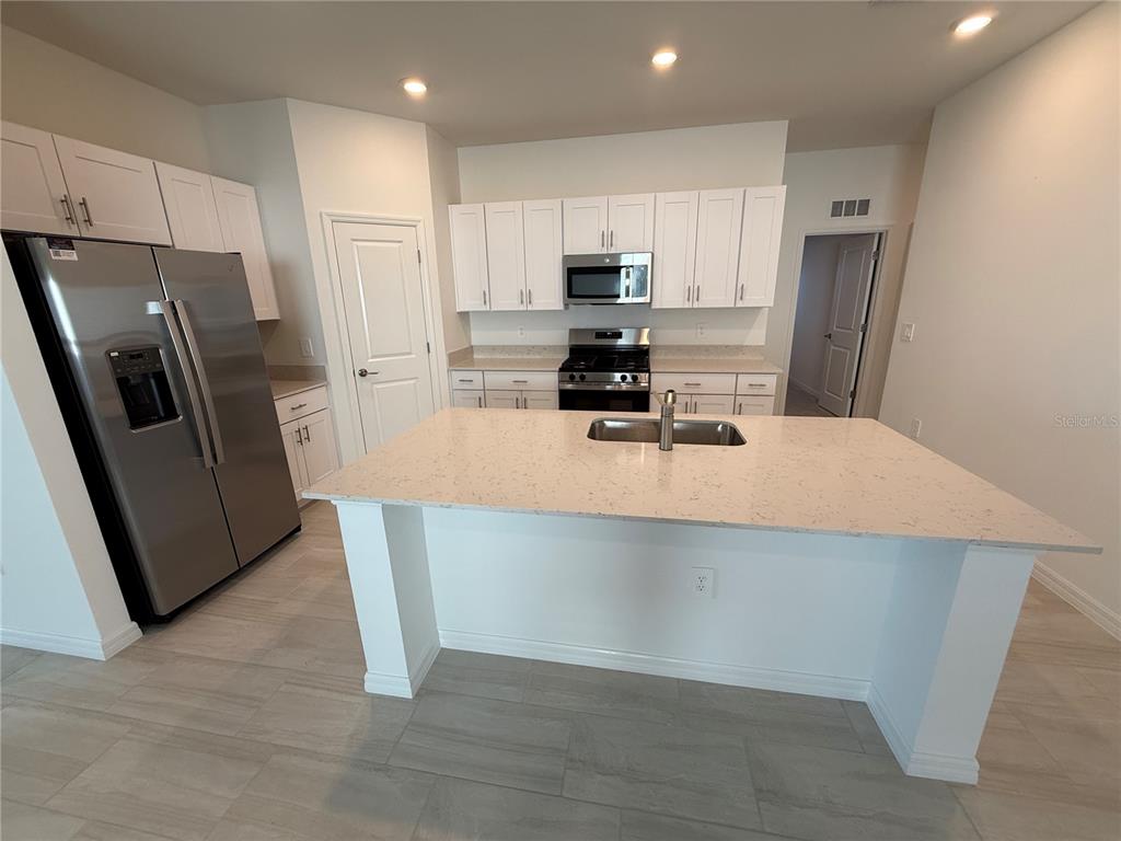 12434 Radiant Crystal Rose Place Parrish, FL 34219 - Photo 5 of 39 a kitchen with stainless steel appliances a refrigerator a sink a stove a microwave and island
