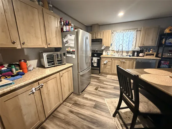 a kitchen with stainless steel appliances granite countertop a refrigerator a sink dishwasher a stove and white countertops with wooden floor