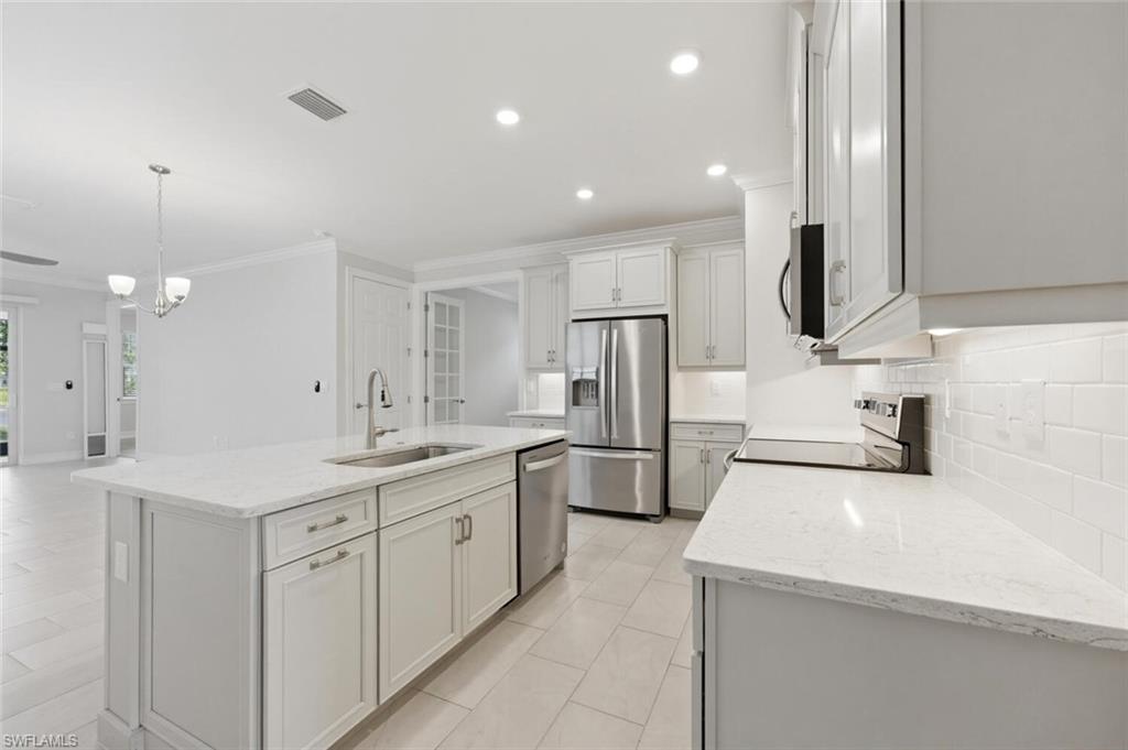 28310 Captiva Shell Loop Bonita Springs, FL 34135 - Photo 11 of 44 Kitchen with light stone counters, tasteful backsplash, ornamental molding, stainless steel appliances, and a center island with sink