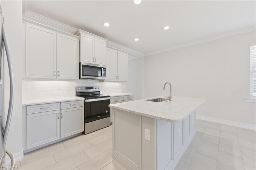 28310 Captiva Shell Loop Bonita Springs, FL 34135 - Photo 10 of 44 Kitchen featuring stainless steel appliances, backsplash, light stone countertops, a center island with sink, and ornamental molding