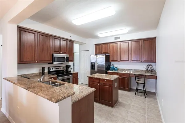 a kitchen with stainless steel appliances granite countertop a stove top oven a sink dishwasher and a refrigerator with wooden cabinets