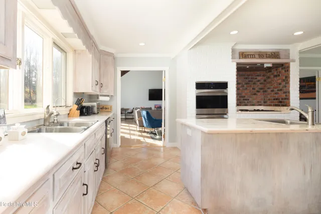 a large white kitchen with stainless steel appliances a large counter top a stove a chimney a sink and a large window