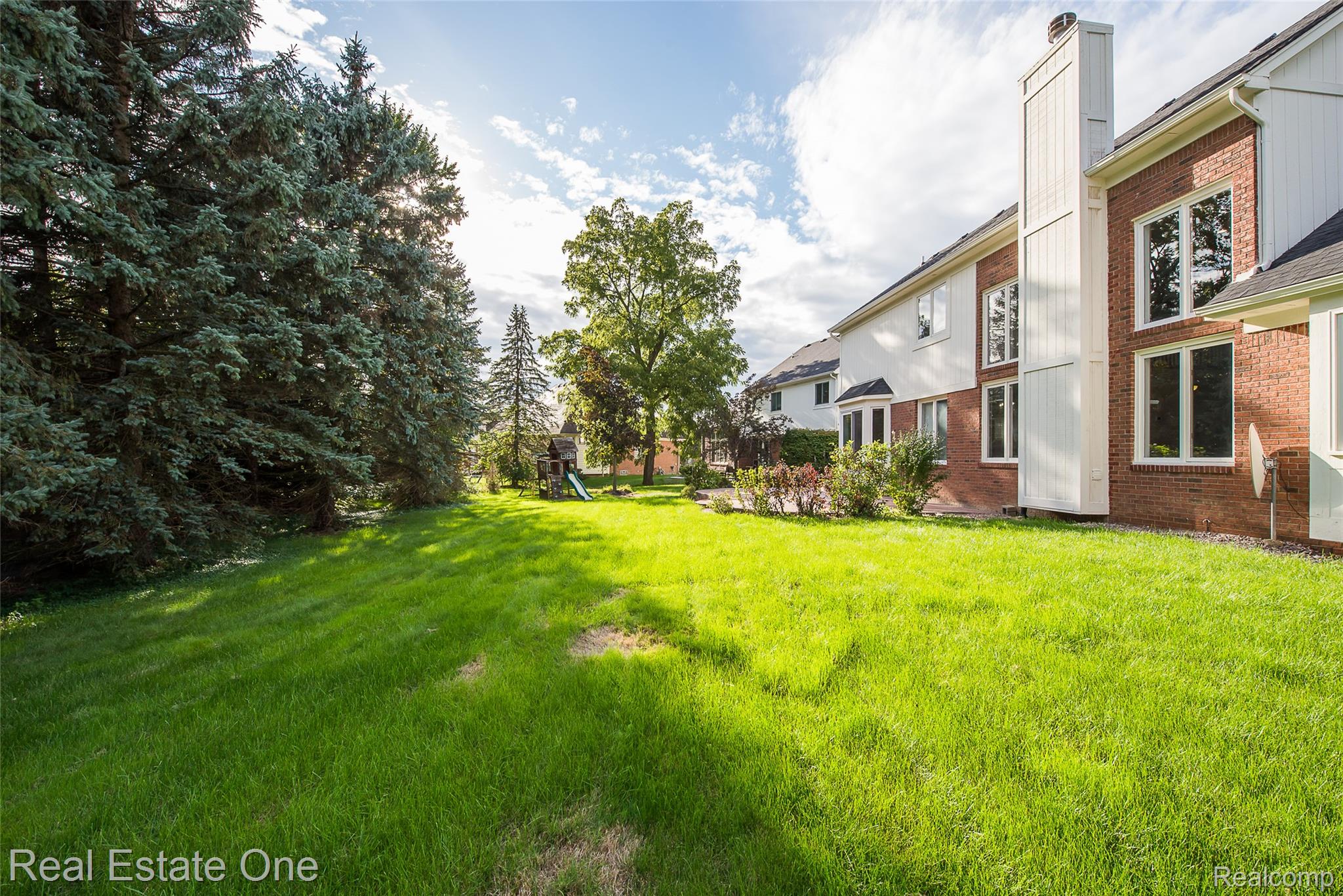 1013 Rochelle Park Drive Rochester, MI 48307 - Photo 68 of 74 Expansive green lawn with mature evergreen trees and a brick and siding exterior