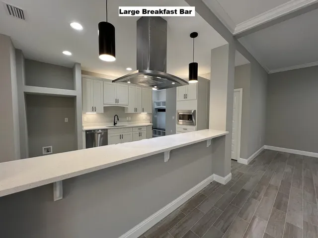 a large kitchen with stainless steel appliances a large counter top a stove and a wooden floors