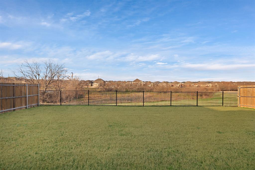 3204 Renaissance Drive Denton, TX 76207 - Photo 25 of 25 Expansive rear lawn featuring a metal perimeter fence, wood panel fencing, and distant residential structures