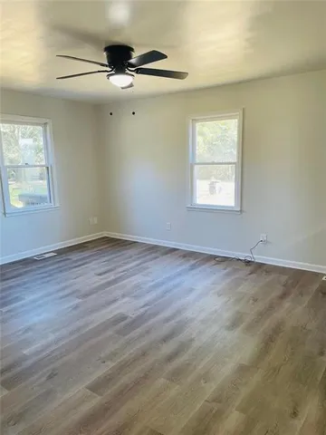 an empty room with wooden floor fan and windows