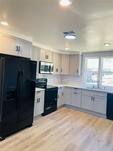 a large kitchen with stainless steel appliances granite countertop a refrigerator a sink dishwasher a stove and white cabinets with wooden floor