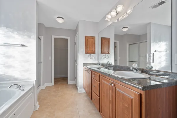 a spacious bathroom with a granite countertop double vanity sink a large mirror and a bathtub