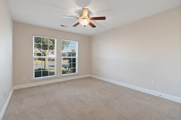 an empty room with ceiling fan and windows