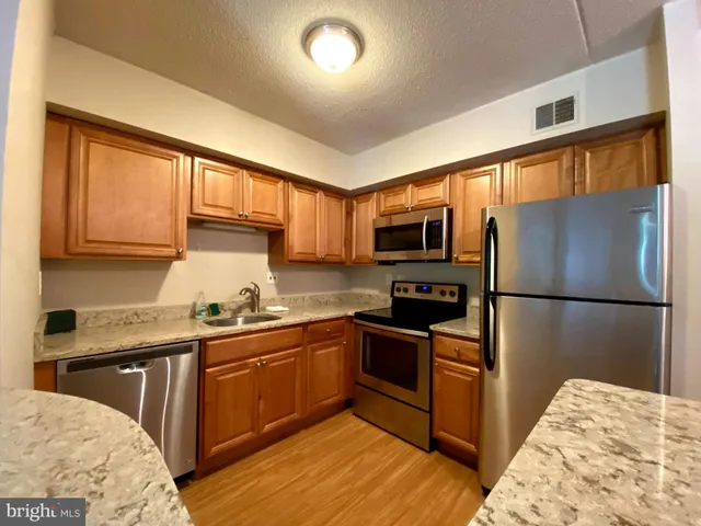 a kitchen with stainless steel appliances granite countertop a refrigerator a sink dishwasher a stove with wooden cabinets and floor