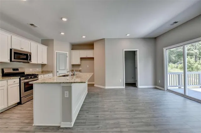 a kitchen with stainless steel appliances granite countertop a stove top oven a sink dishwasher a refrigerator and a microwave oven with wooden floor