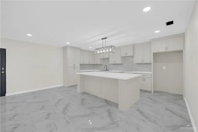 a large white kitchen with kitchen island a sink stainless steel appliances and cabinets