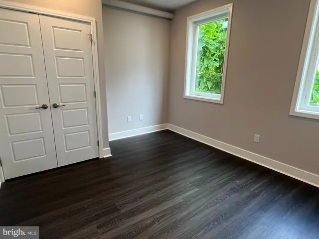 an empty room with wooden floor closet and windows