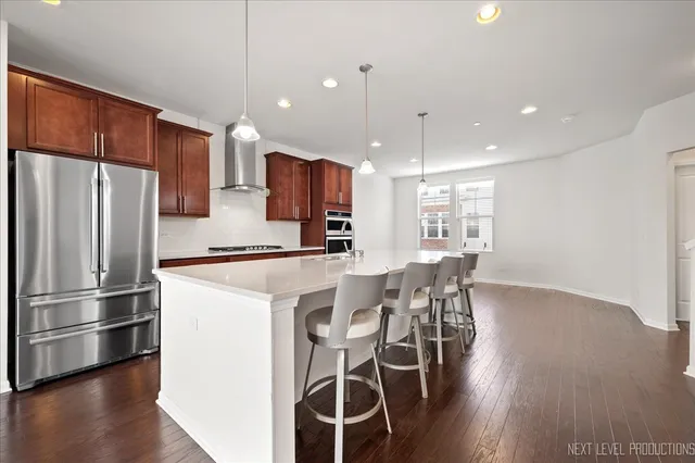 a kitchen with stainless steel appliances a dining table chairs refrigerator and wooden floor