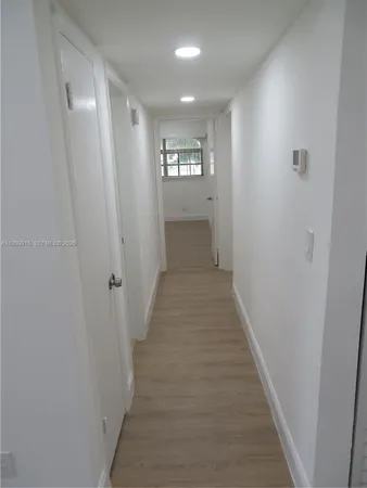 a view of a hallway with wooden floor and a bathroom