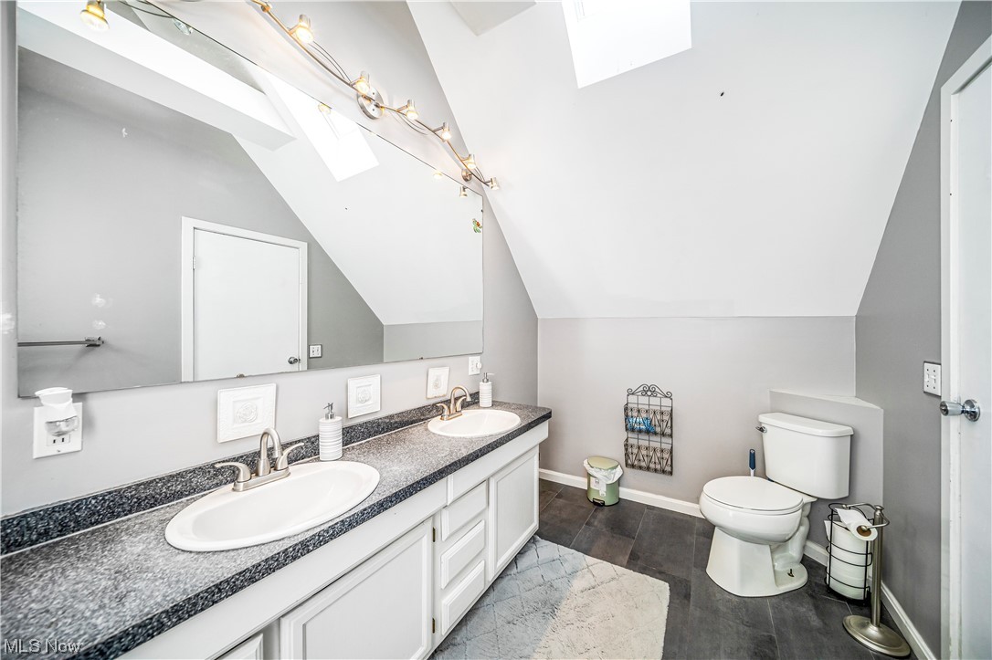 3211 River Road Perry, OH 44081 - Photo 18 of 34 Bathroom featuring toilet, double sink vanity, and vaulted ceiling with skylight