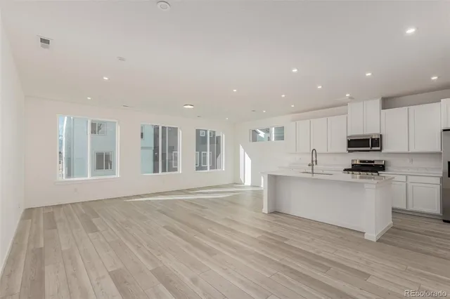 a large white kitchen with kitchen island a stove a sink dishwasher and white cabinets with wooden floor