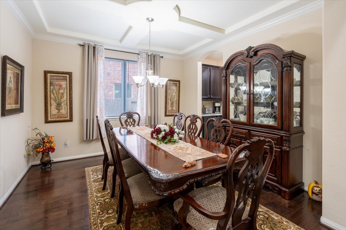This dining room features elegant dark wood furniture, including a large table and china cabinet. It has a sophisticated chandelier, decorative ceiling, and a window providing natural light. The space is accented with framed artwork and a patterned rug, creating a warm and inviting atmosphere.