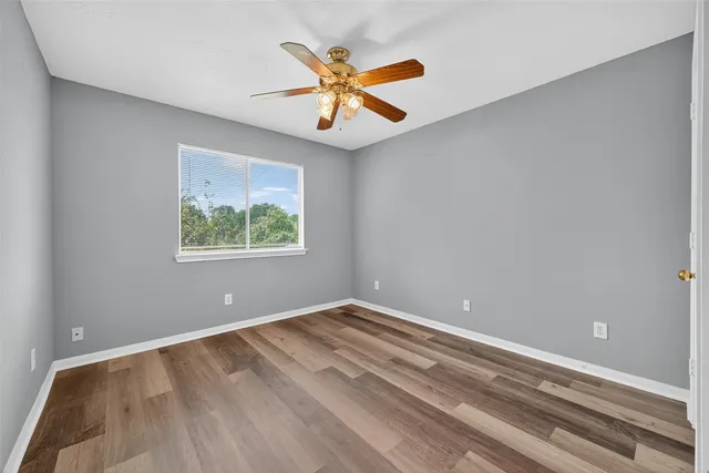 an empty room with wooden floor ceiling fan and windows