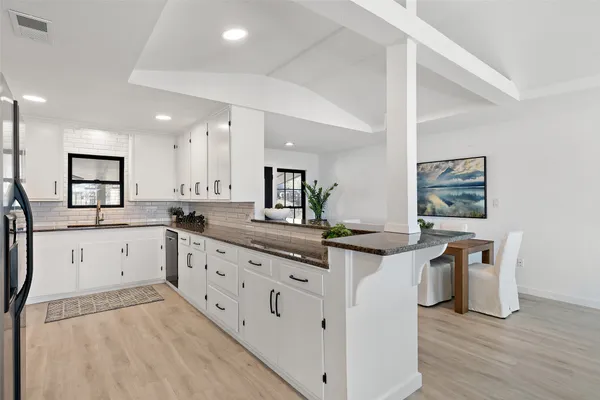 a large white kitchen with stainless steel appliances granite countertop a lot of counter space and wooden floors