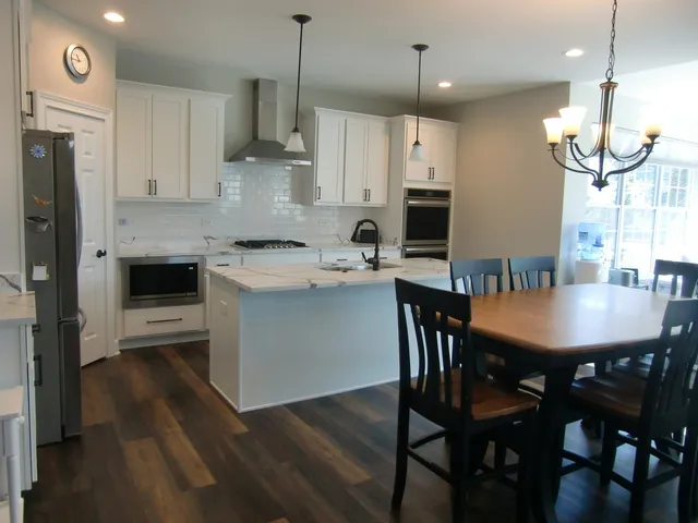 a kitchen with stainless steel appliances granite countertop a stove a refrigerator a kitchen island a dining table and chairs with wooden floor